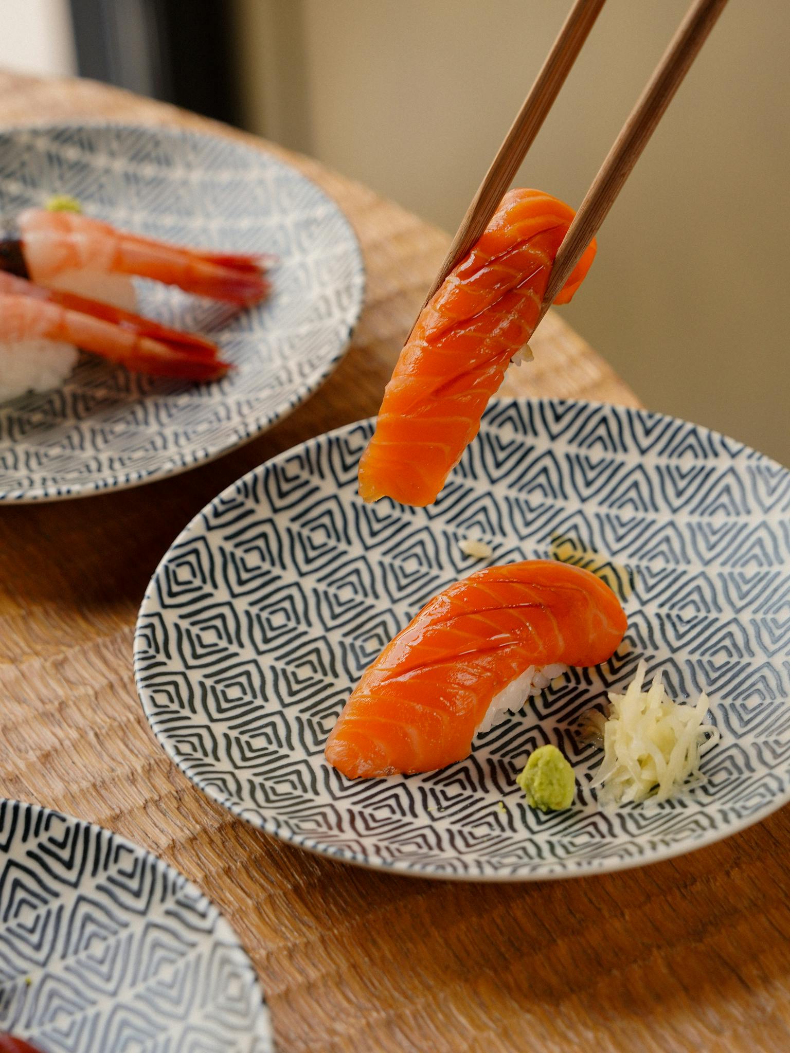 Close-up of salmon nigiri sushi on patterned plates with chopsticks, showcasing Japanese cuisine.